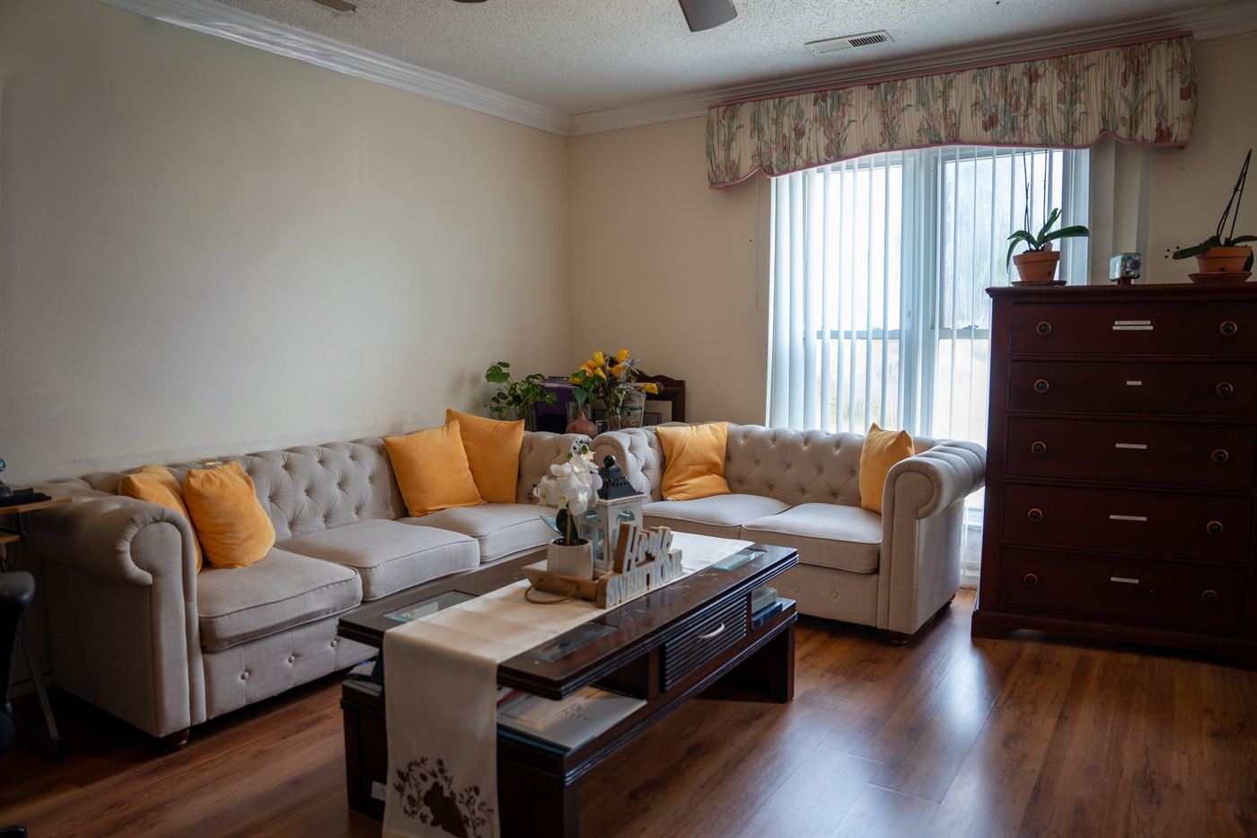 The living room at Comfort Living — cream sectional sofa with mustard accent pillows, family-style coffee table with fresh flowers, sunlit window